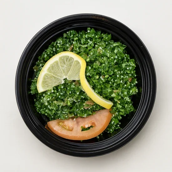 Kale salad with lemon wedge and tomato slice in a black bowl