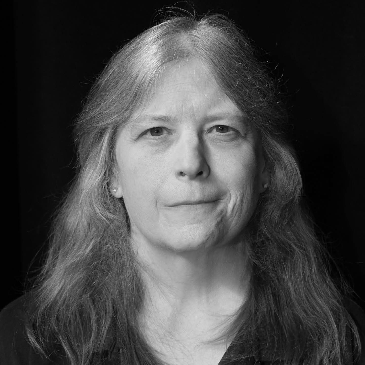 Black and white portrait of a woman with long hair, wearing earrings, looking at the camera with a neutral expression.