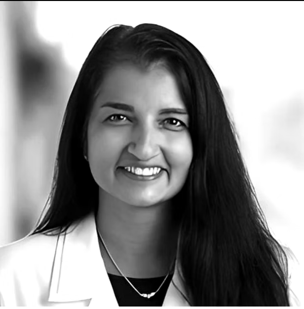 Black and white portrait of a smiling woman with long dark hair wearing a white blazer and a necklace.