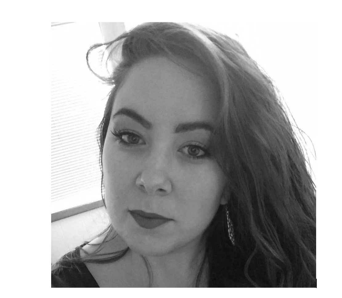 A black and white photo of a woman with long, wavy hair, wearing makeup, earrings, and a dark top, looking slightly to the left with a serious expression.