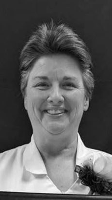 Black and white portrait of a smiling woman with short hair, wearing a white blouse, with a flower pinned near her collar.