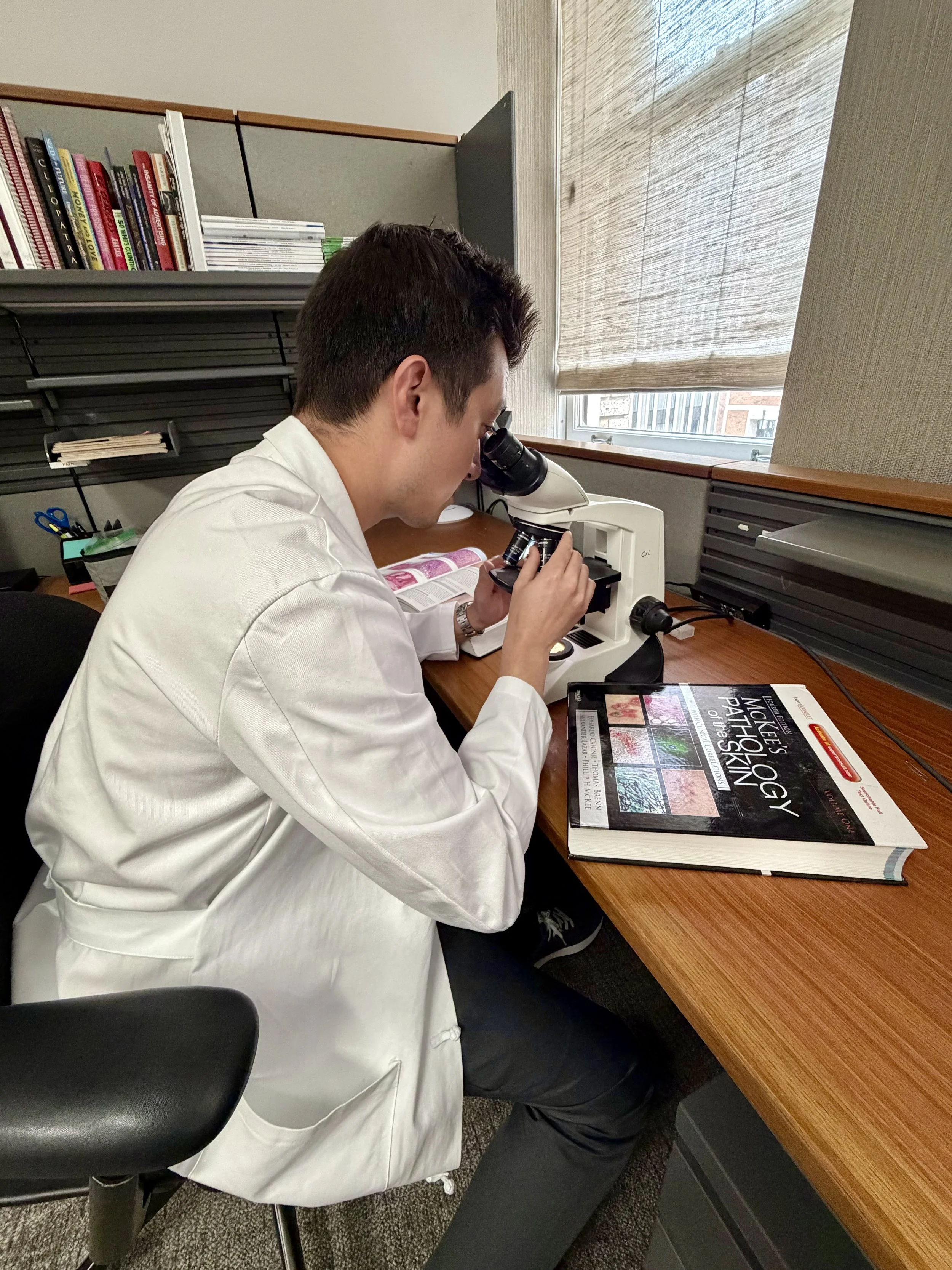 Dr. Edward K. Hadeler reviewing dermatopathology slides under the microscope.