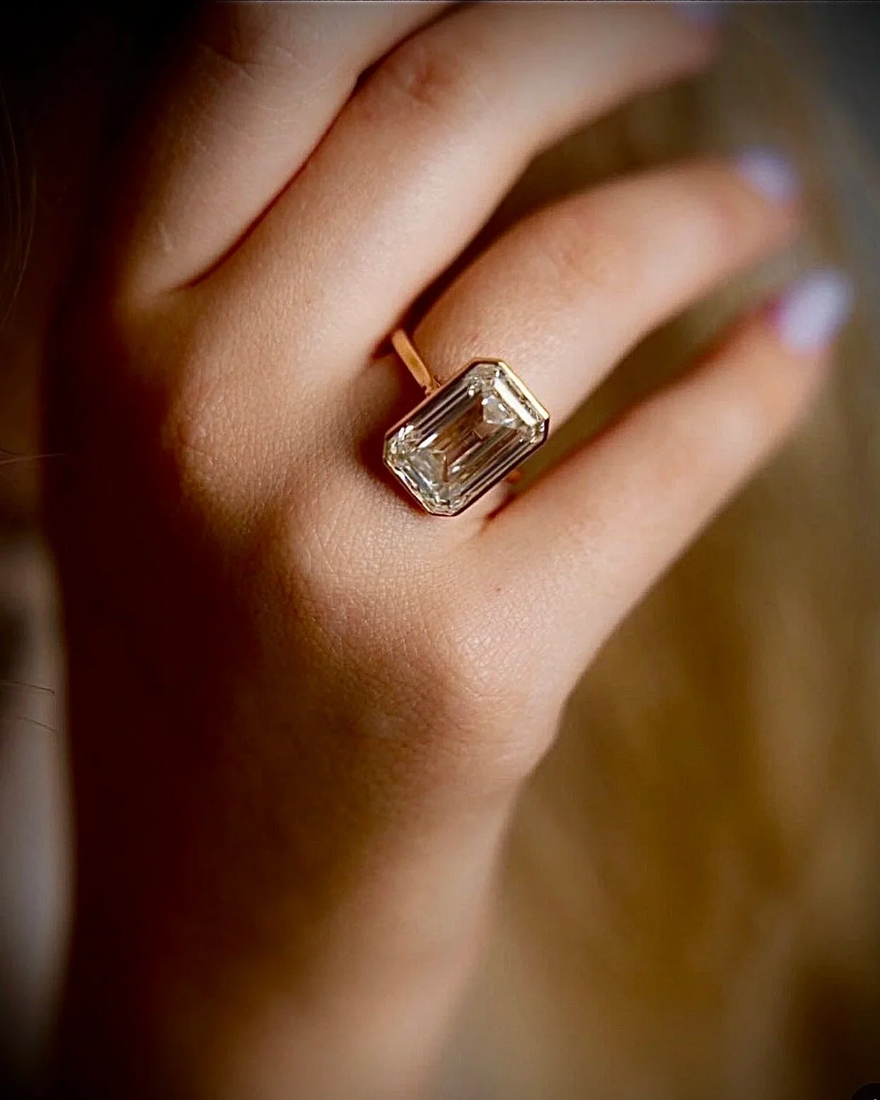 Close-up of a person's hand showing a large rectangular diamond ring on their finger.
