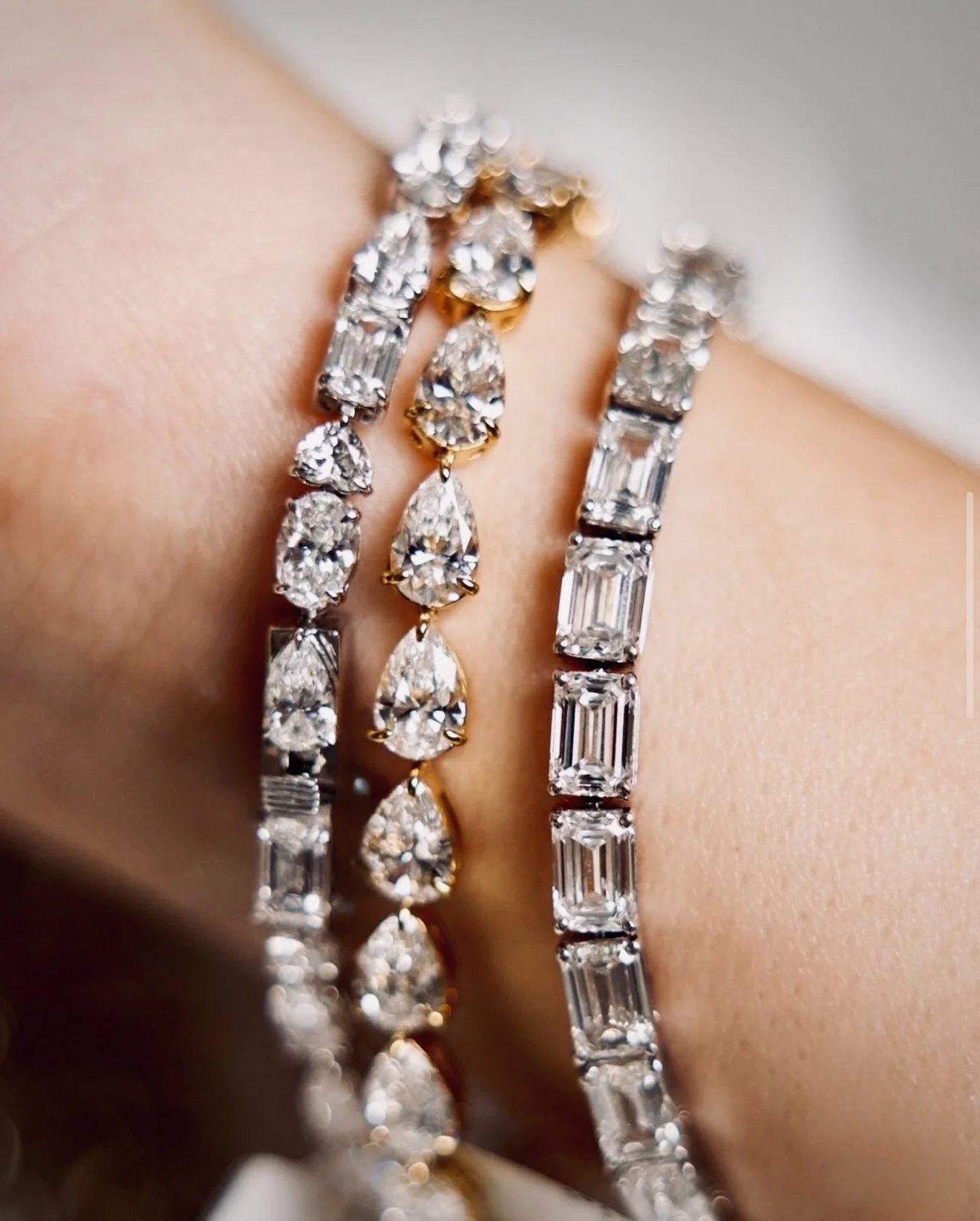 Close-up of a wrist adorned with several luxury diamond bracelets, featuring various cuts and settings.