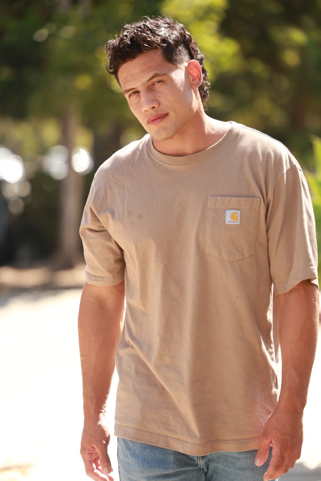 Artist wearing a beige Carhartt T-shirt standing outdoors in natural sunlight.