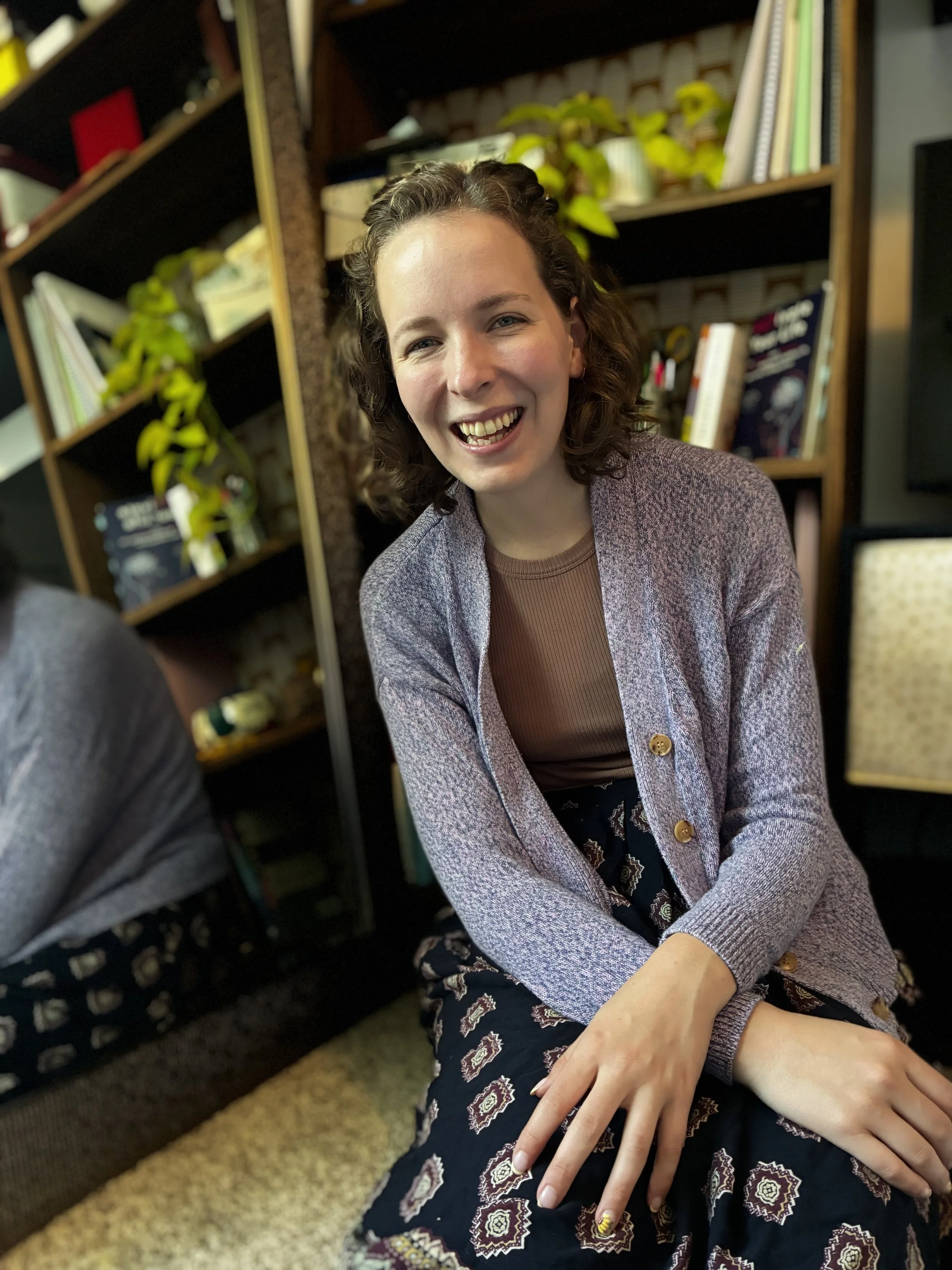 Maddi, wearing a purple cardigan, seating, smiling
