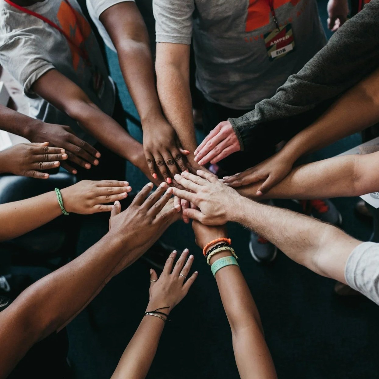 Multiple hands of diverse people stacked together in a gesture of solidarity and unity.