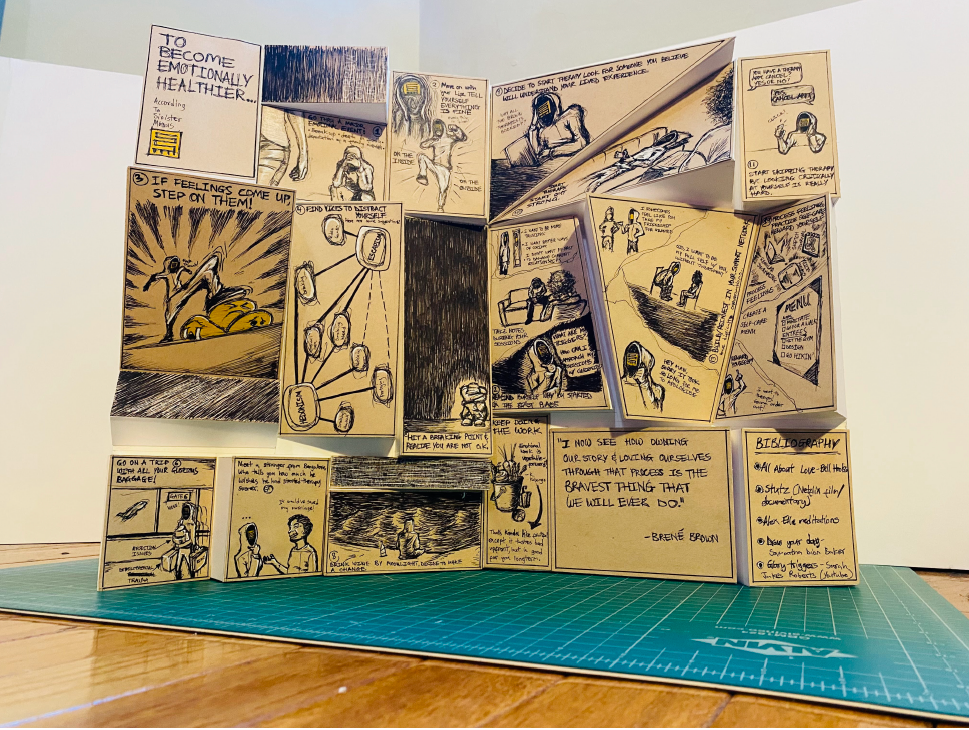 A detailed 3D paper model of a multi-panel comic strip on a green cutting mat, depicting various scenes and quotes about emotional health and self-improvement, with handwritten text and illustrations in black ink on beige paper.
