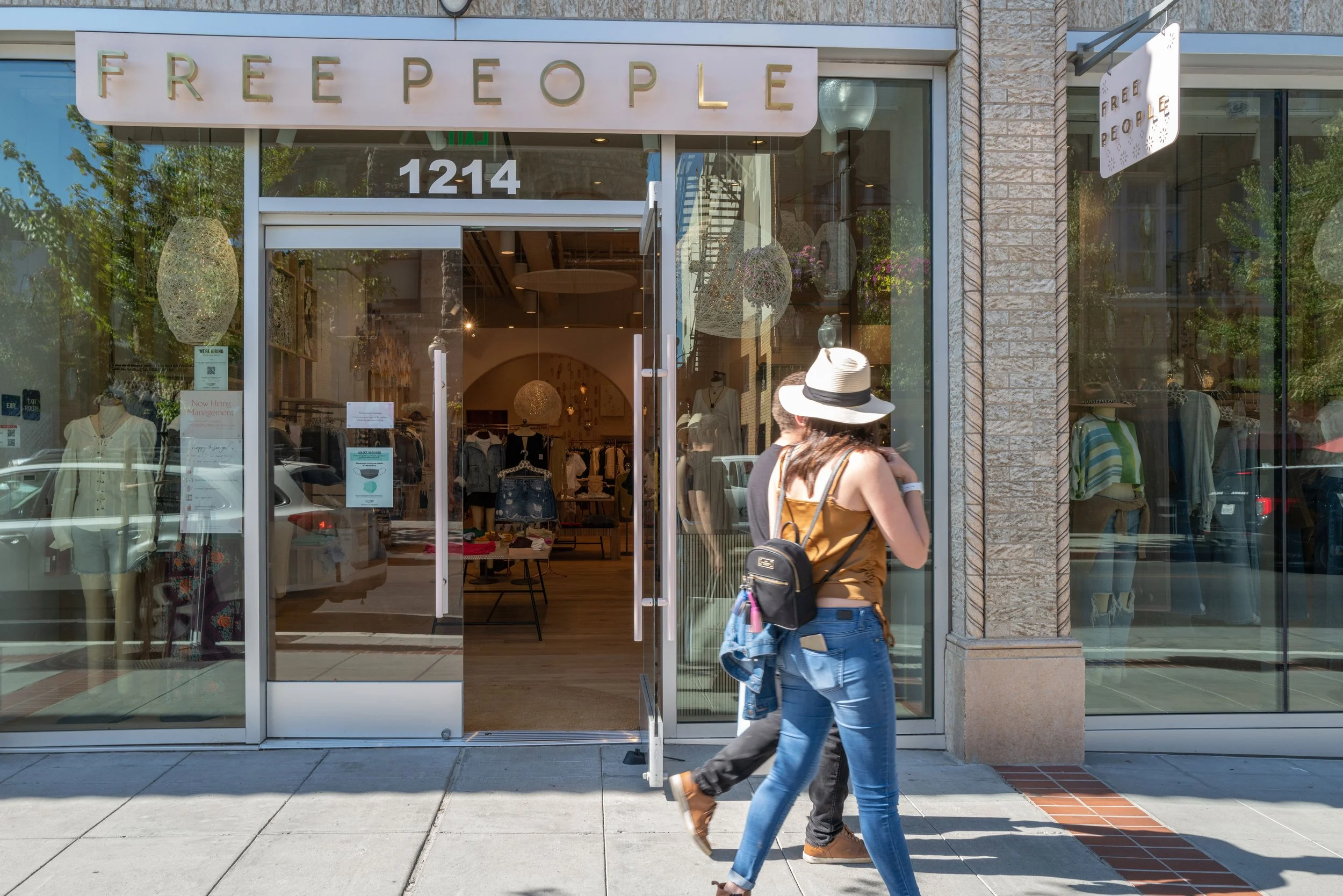 People walking past a clothing store with a sign that says 'FREE PEOPLE' on the storefront.