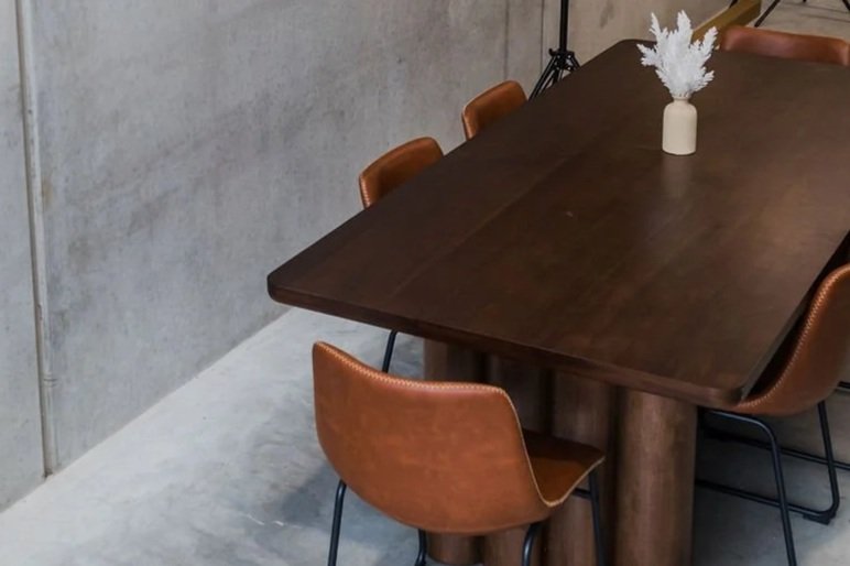 Wood dining table with six brown leather chairs and a white vase with white pampas grass centerpiece.