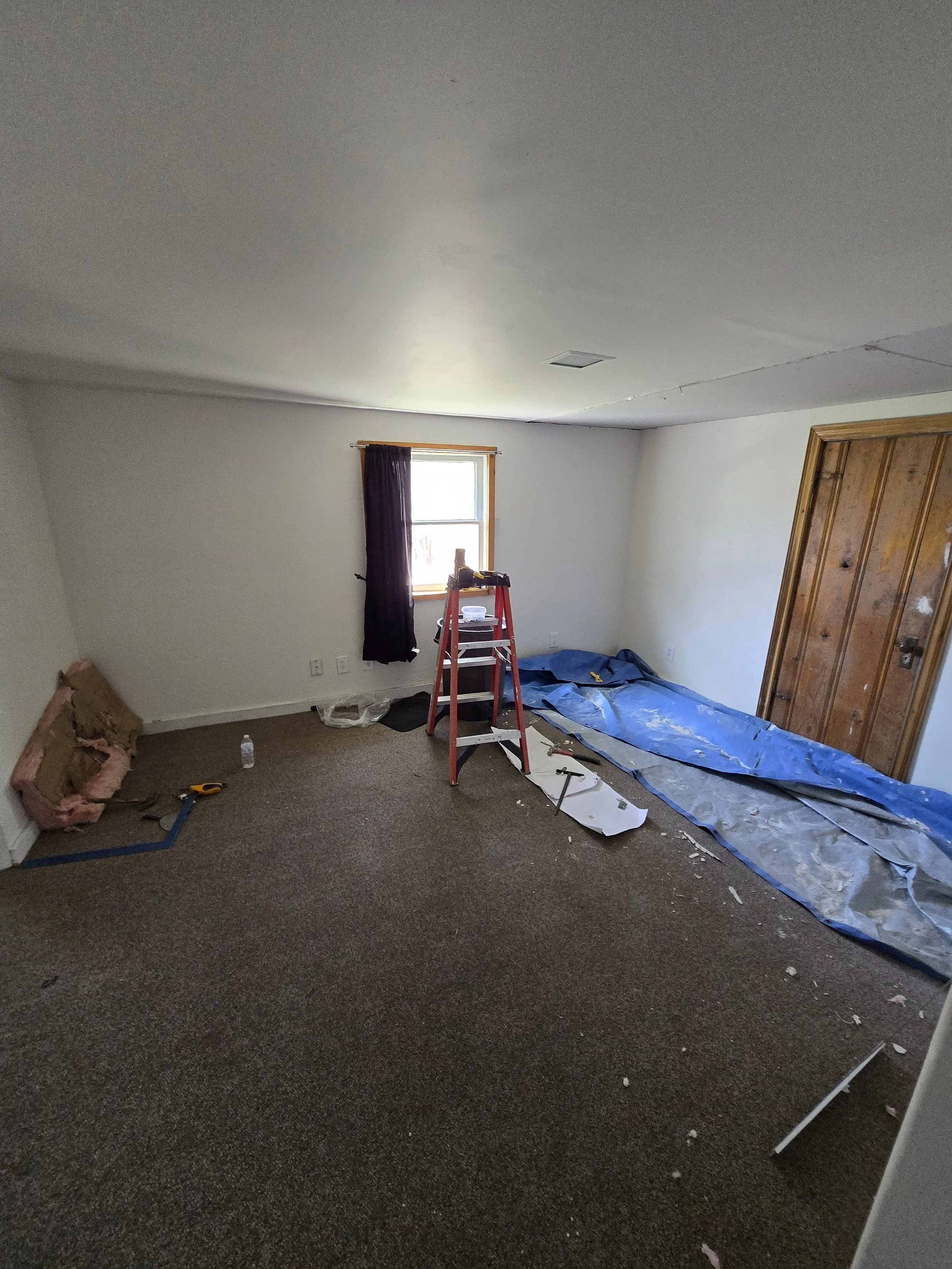 Room undergoing renovation with tools, electrical wires, a ladder, a plastic sheet on the floor, and an open closet door.