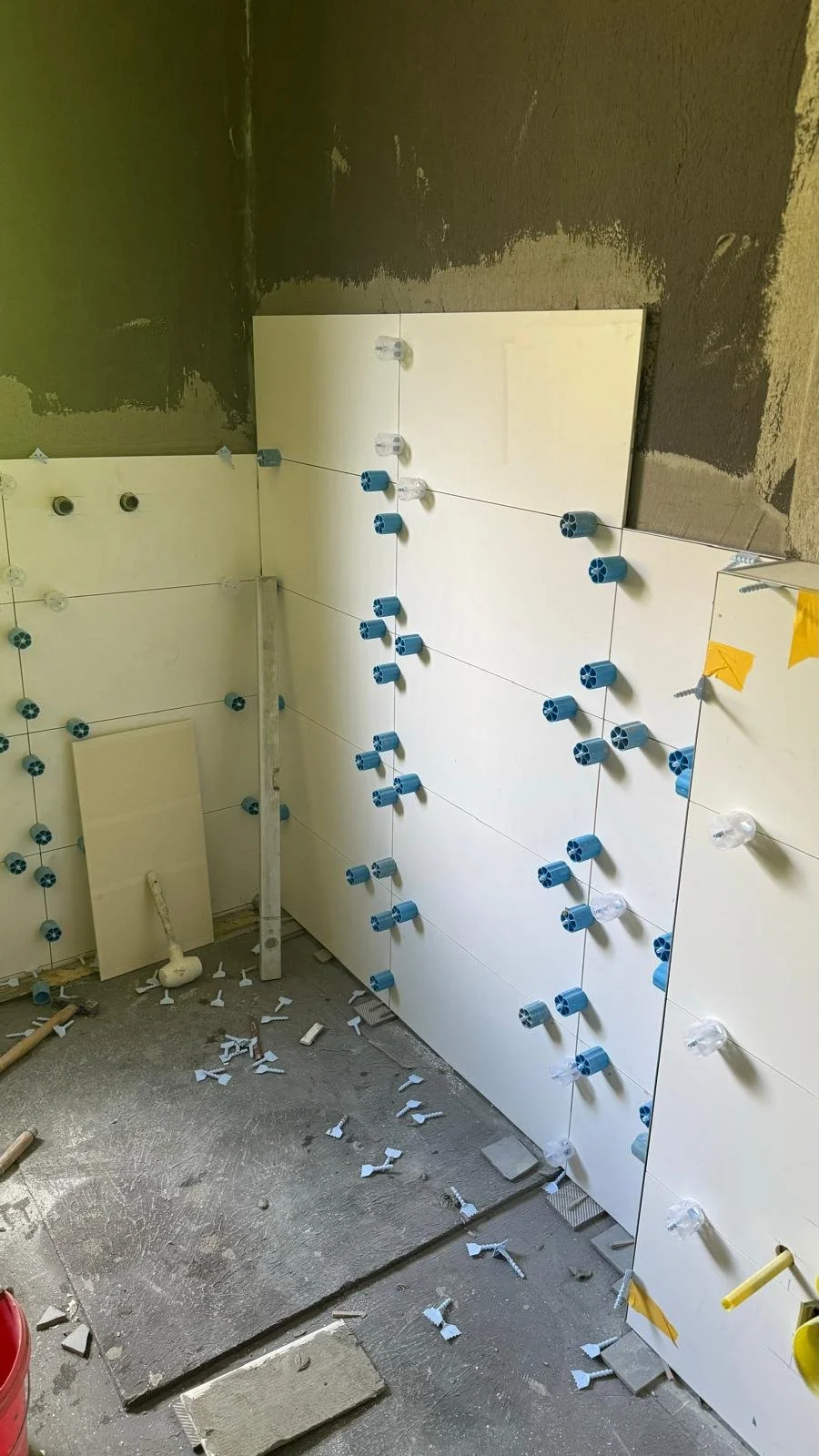 Mauer mit Fliesen, die mit Klemmen für die Flieseninstallation befestigt werden, in einem Renovierungsraum.