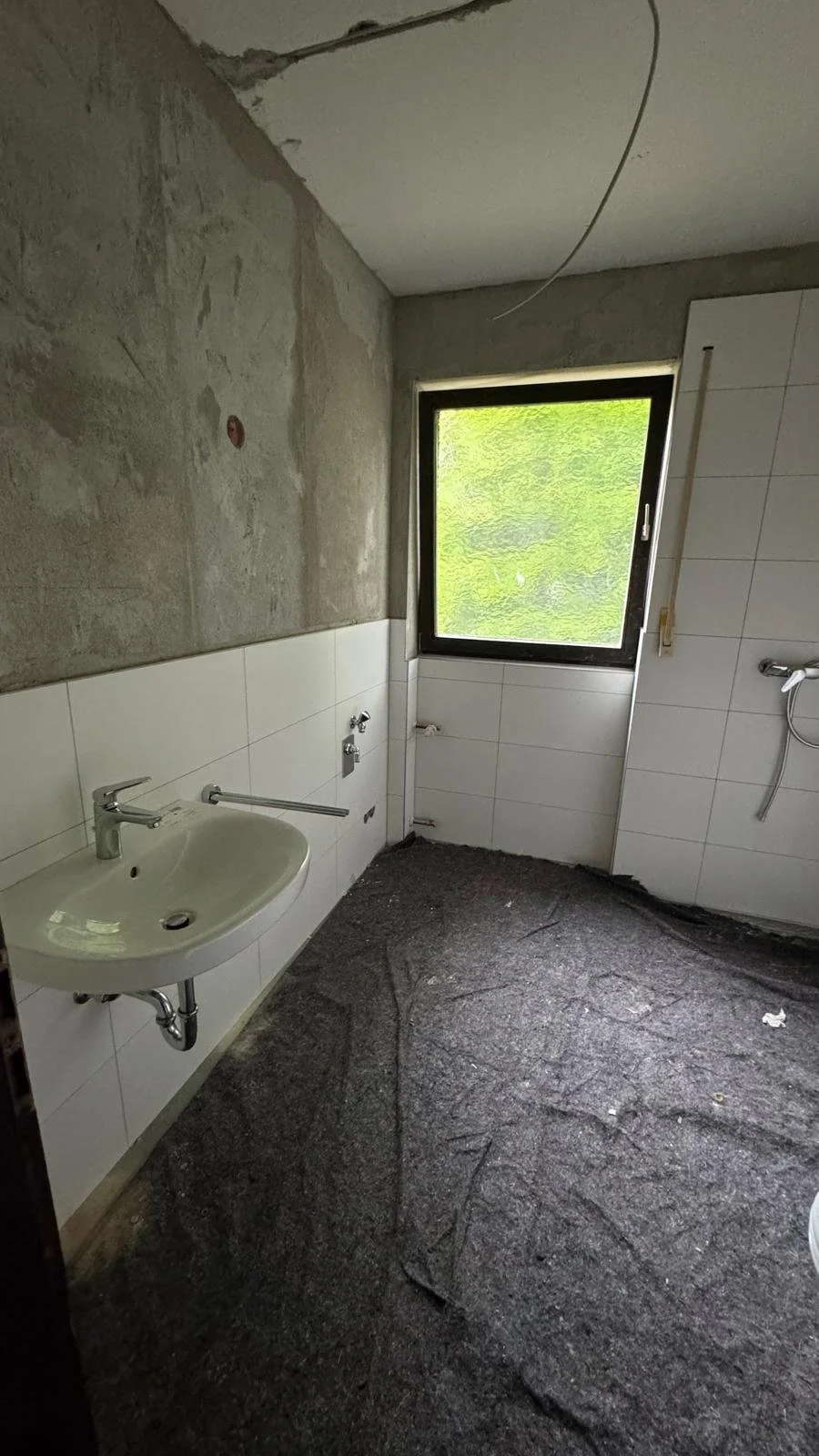 Ein Badezimmer im Bau mit weißen Wandfliesen, einem Waschbecken, einem Fenster und unvollständiger Installation.