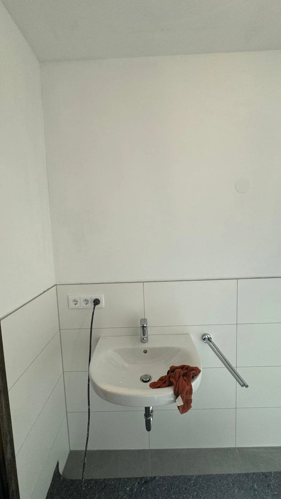 Waschbecken in einem Badezimmer mit einem Wasserhahn, einem Handtuch und einer Ablage, Steckdosen und eine blinde Ecke.