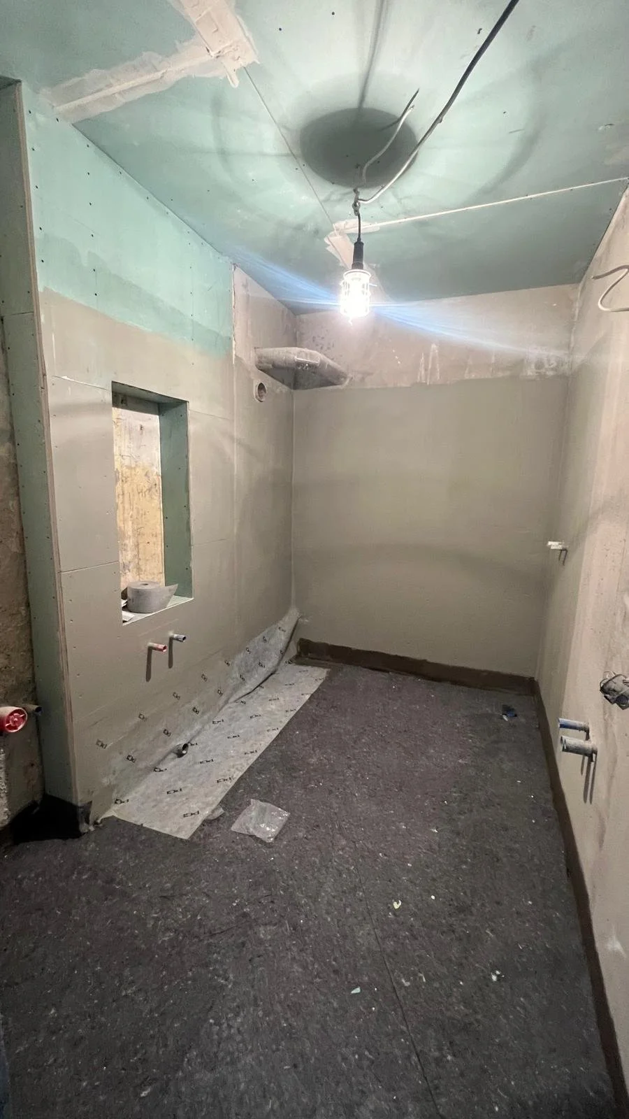 Ein Badezimmer im Bauzustand mit unvollständigen Wänden, einer Decke, die noch isoliert wird, einer unvollständigen Wasser- und Elektrikinstallation, und einem schwebenden Arbeitsscheinwerfer an der Decke.