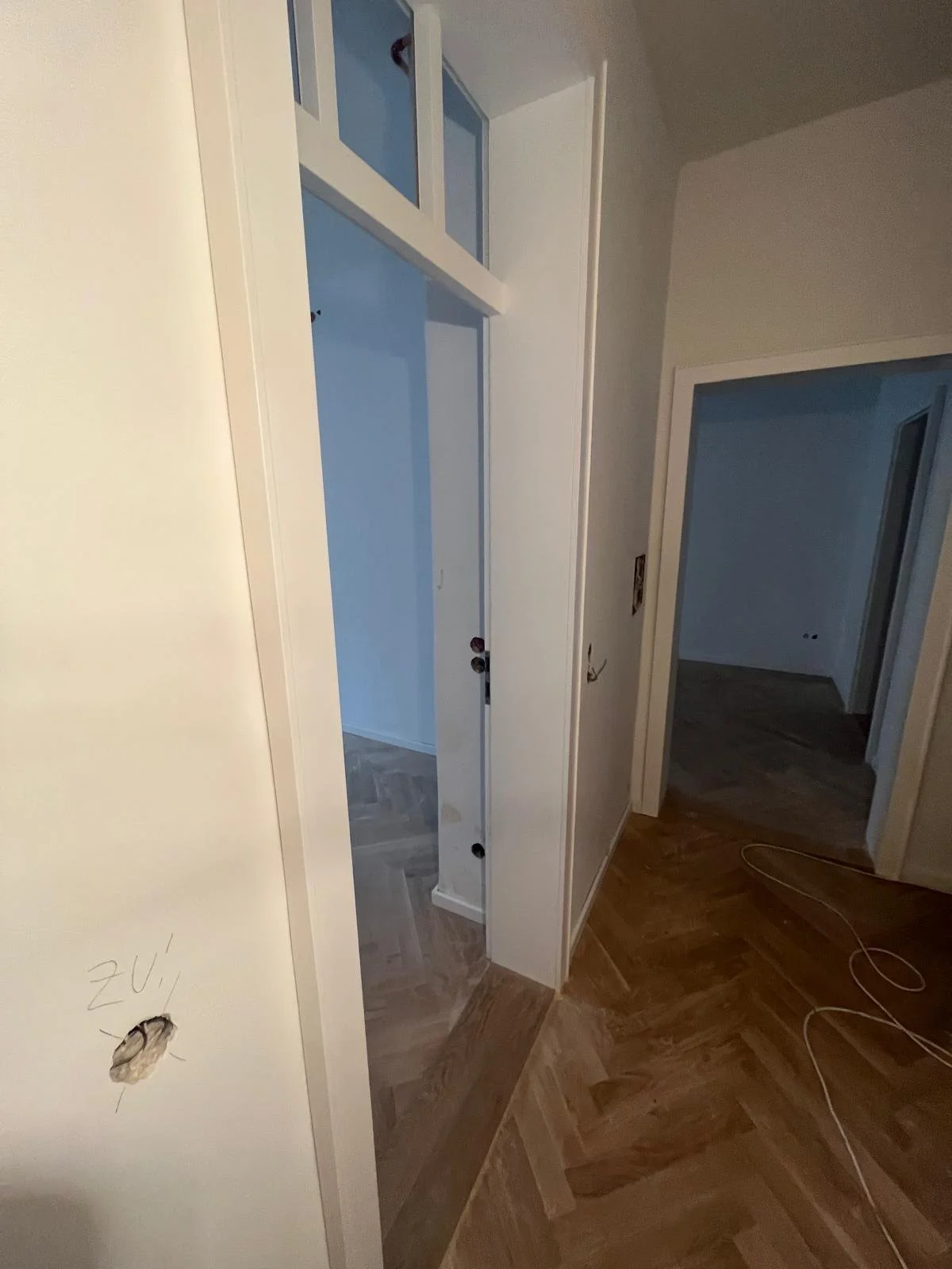 Innenansicht eines verlassenen Gebäudes mit weißen Wänden, Türen und einer Holzbodenverlegung.