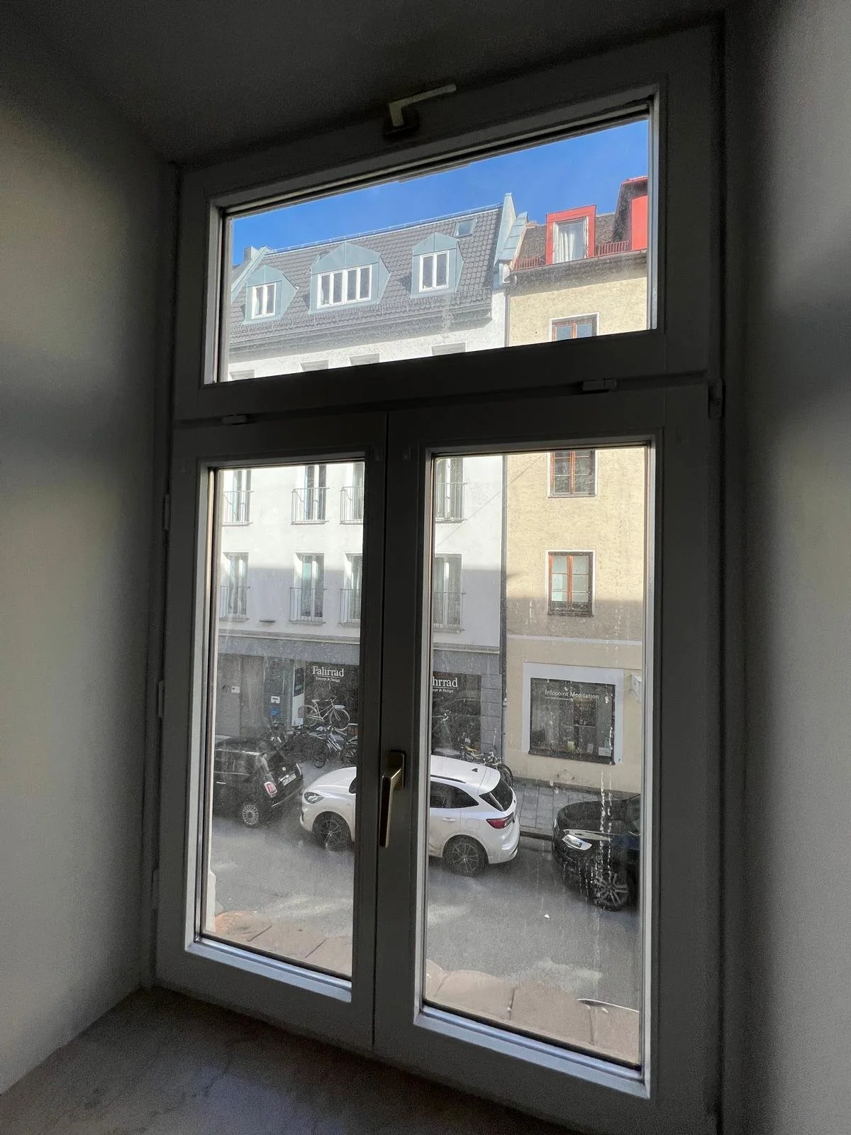 Blick durch eine Fensterfront auf die Straße mit geparkten Autos und gegenüberliegenden Gebäuden