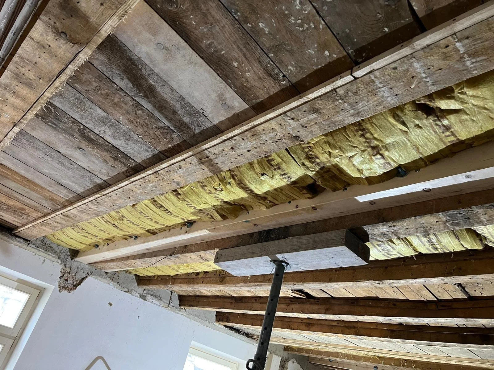 Decke eines Zimmers mit sichtbaren Holzbalken und Dämmmaterial zwischen den Balken.