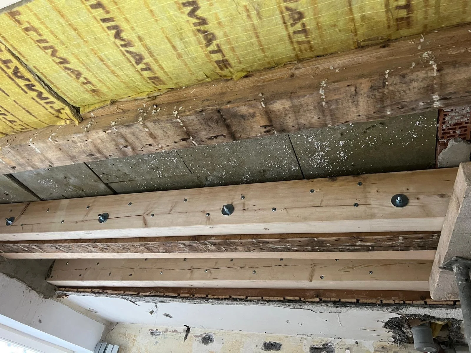 Unterschiedliche Holz- und Dämmmaterialien werden an der Decke eines Raumes befestigt, inklusive Holzlatten, Dämmwolle und Schrauben.