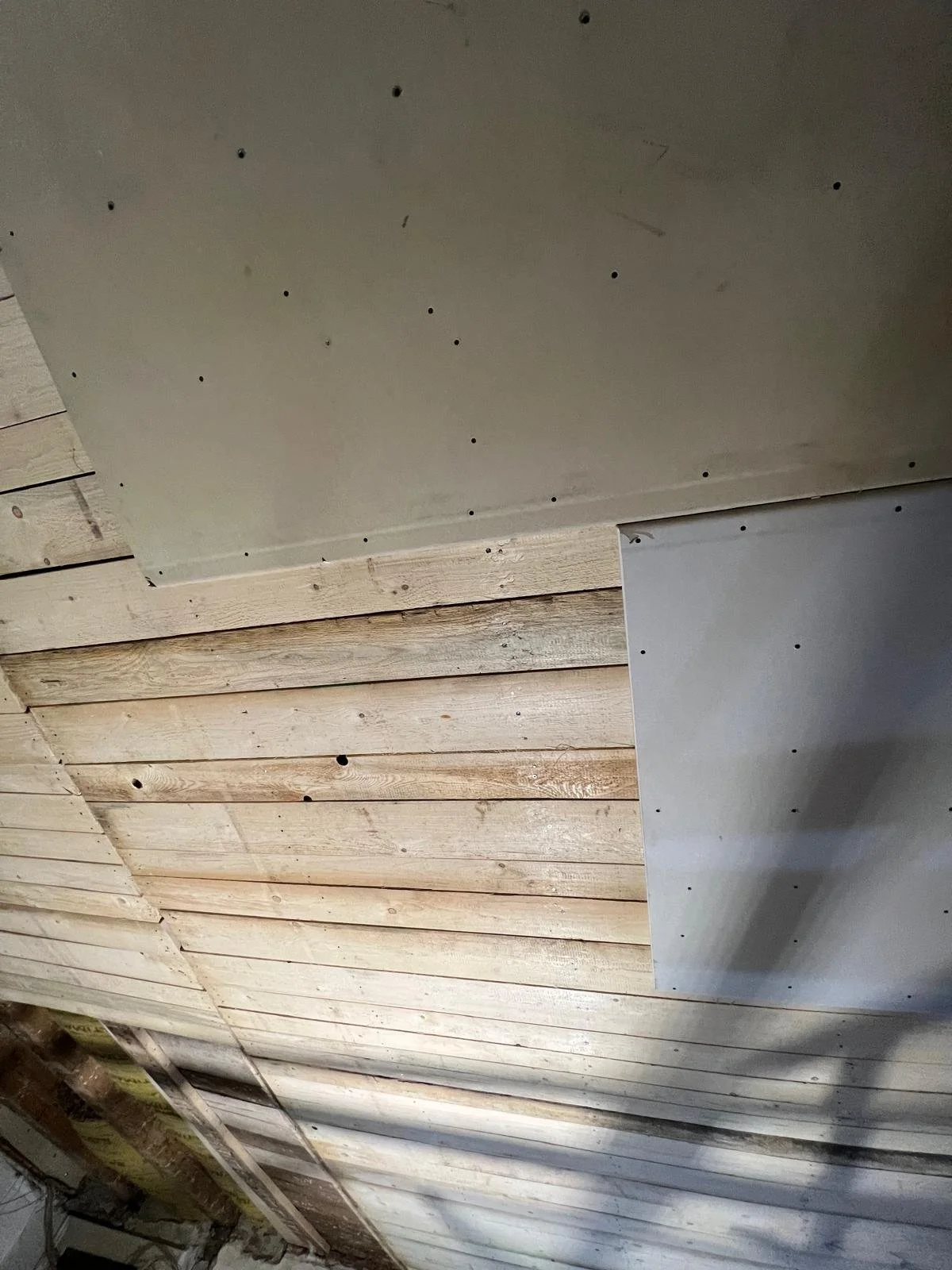 Holzdecke mit eingebauten Trockenbauplatten, die an Schrauben befestigt sind, in einem Raum im Bau.