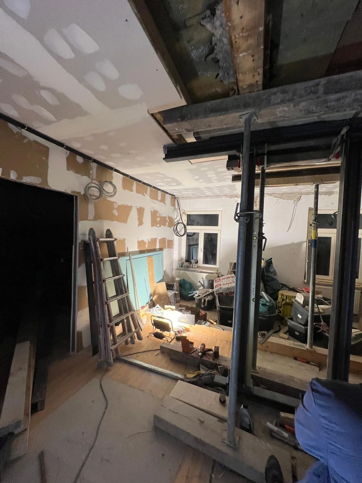 Innenraum eines Raumes wird renoviert, mit aufgebauter Leiter, Baugerüst, Werkzeugen, Baumaterialien und unvollendeter Wandverkleidung.