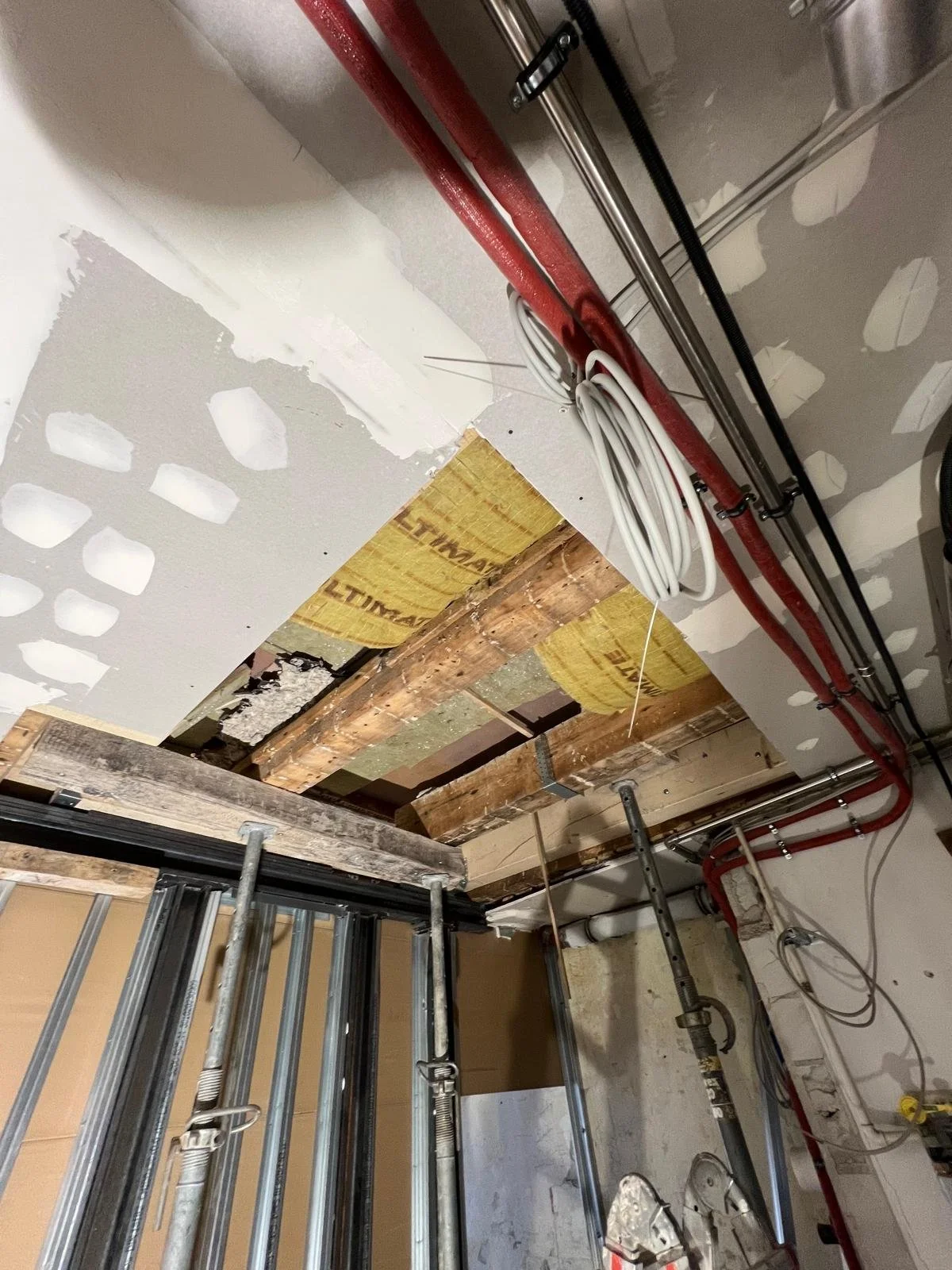 Bauarbeiten im Innenraum mit Rohren und Kabeln, Decke in Bauphase, Holz- und Dämmmaterialien sichtbar.