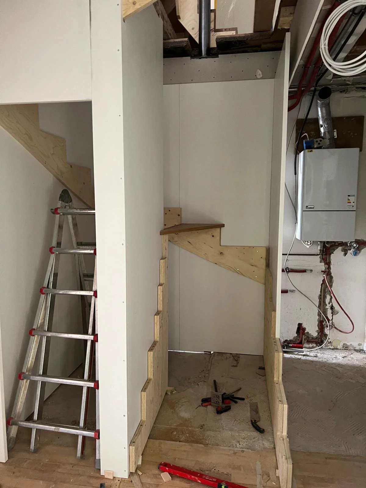 Innenaufnahme eines Bauteilprojektes mit einer kleinen Holztreppe, einer Leiter, Werkzeugen und Rohren