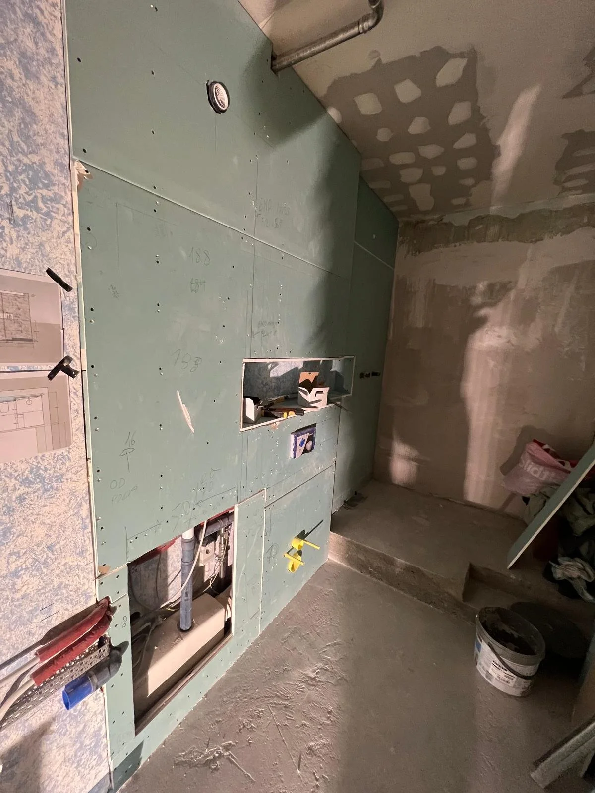 Baustelle mit Wandverkleidung und offener Leitungskasten, im Hintergrund Rohbauwand.