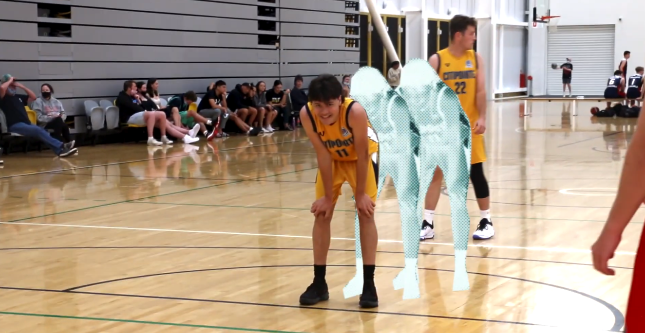 Young basketball players and spectators in a gymnasium, with some players sitting on benches and others standing on the court.