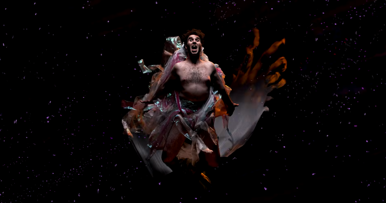 A shirtless man with a surprised or screaming expression surrounded by swirling fabric and particles in a dark, space-like background.