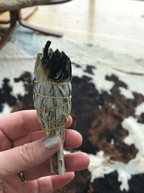 A hand holding a smudged sage bundle wrapped with string.