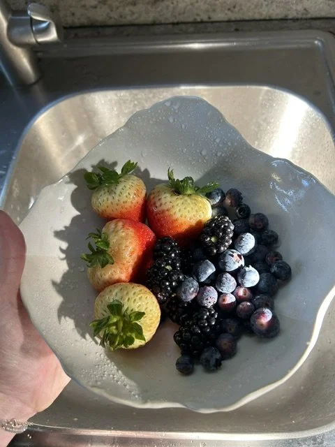 Fresh strawberries and blackberries being washed in a bowl in a kitchen sink.