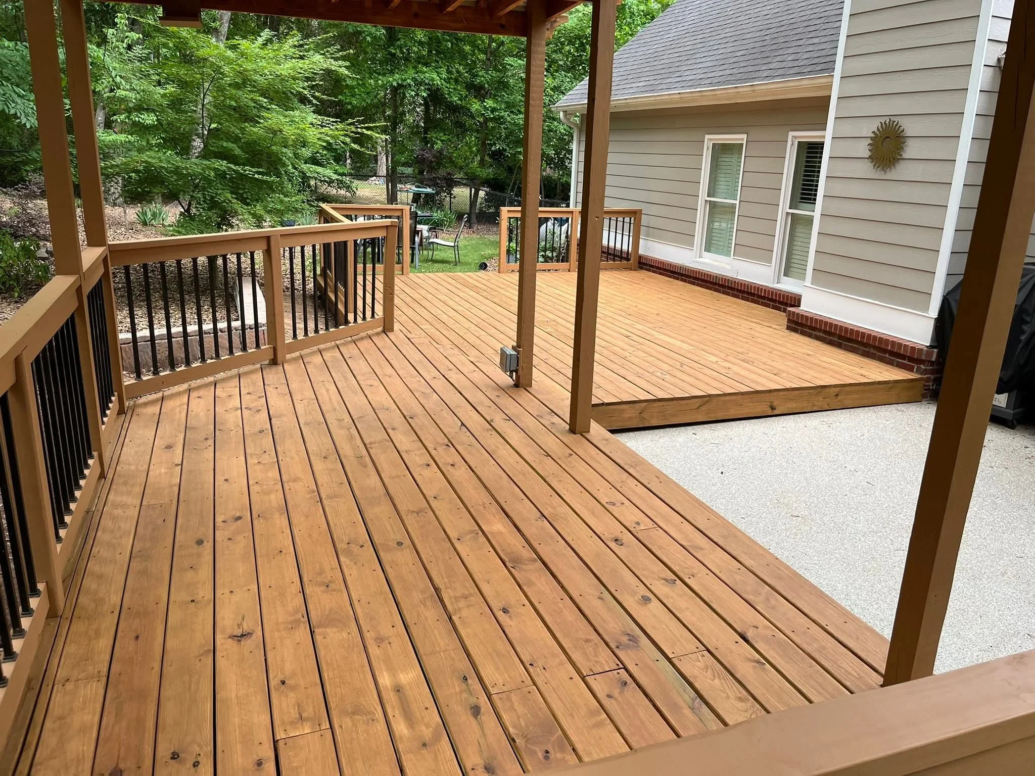 Wooden deck or porch attached to a house, surrounded by trees and greenery.