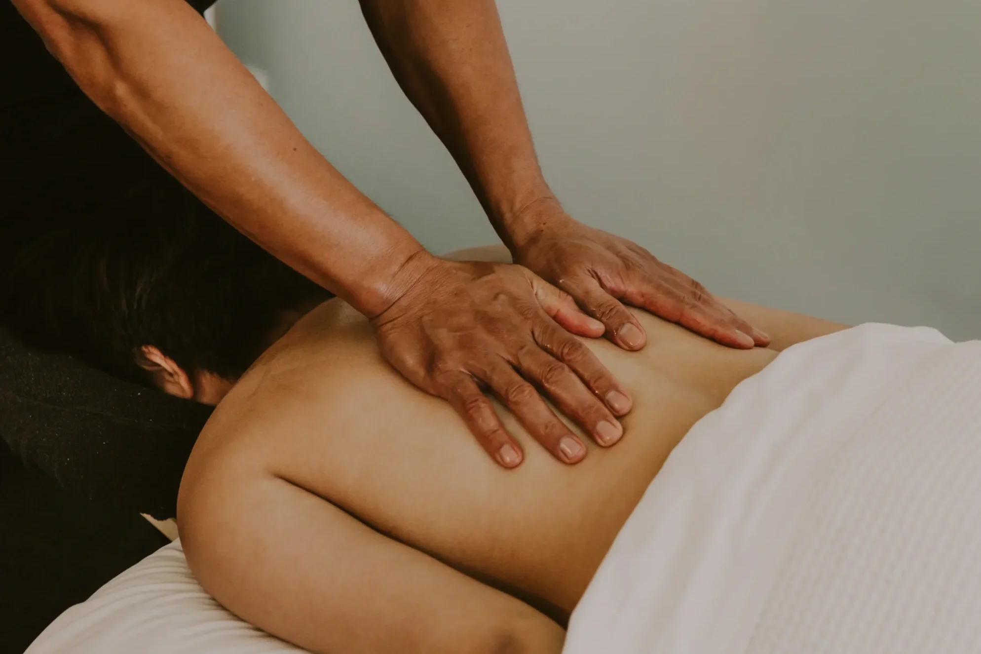 A person giving a massage to another person's back in a massage room.