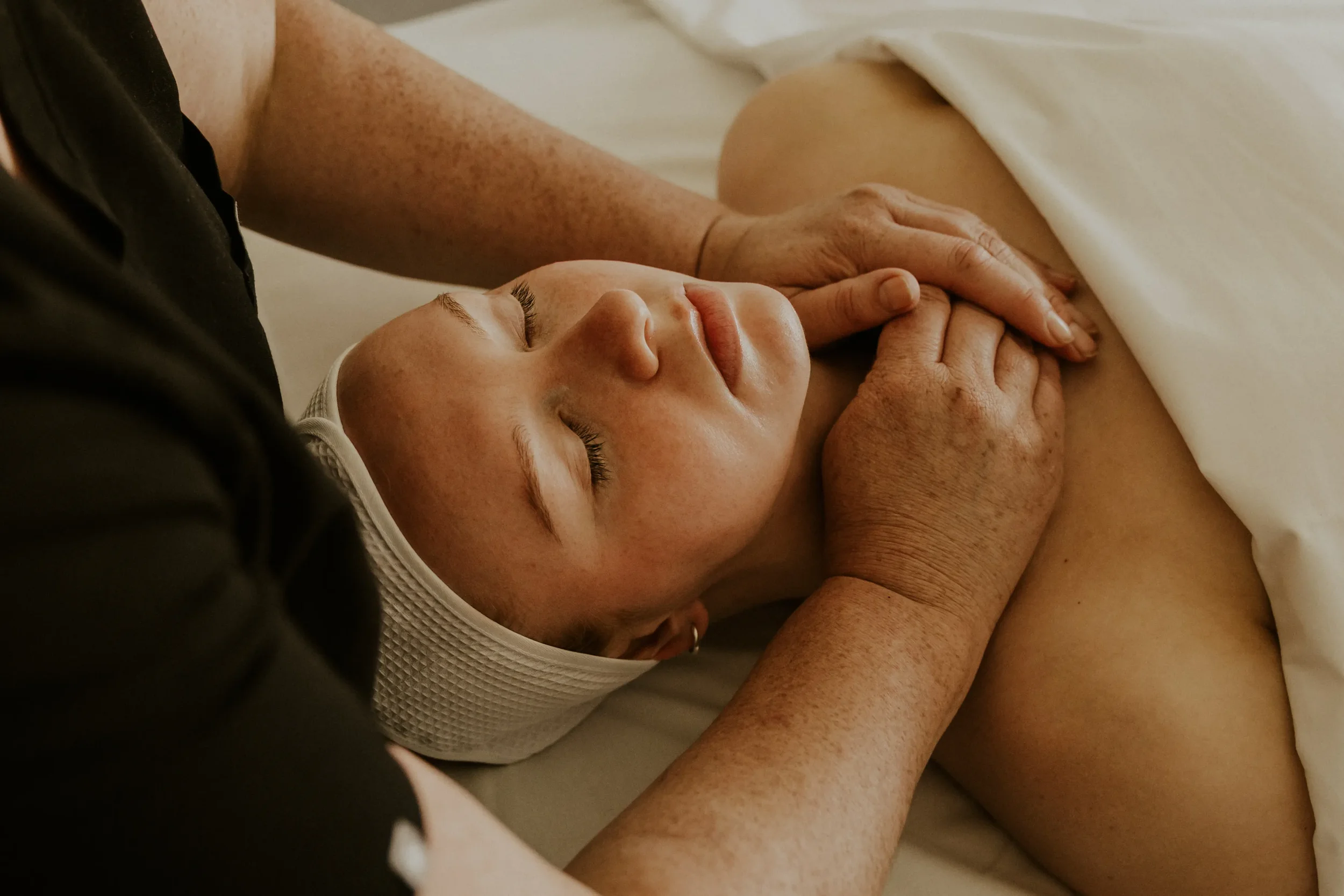 A person receiving a massage, lying face up with eyes closed, with hands gently massaging their chest area.