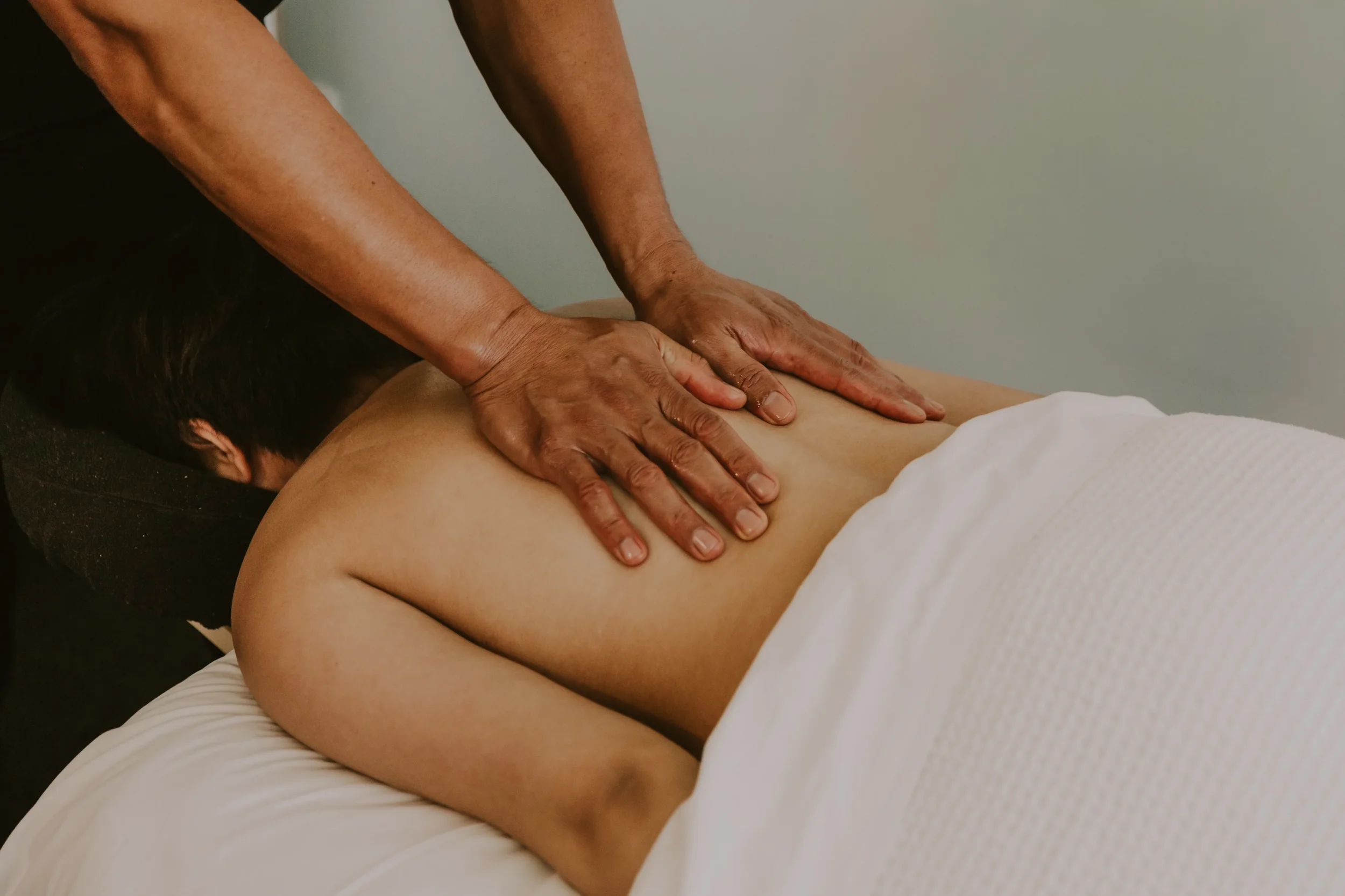 Person receiving a back massage while lying face down on a massage table, with hands applying pressure to their back.