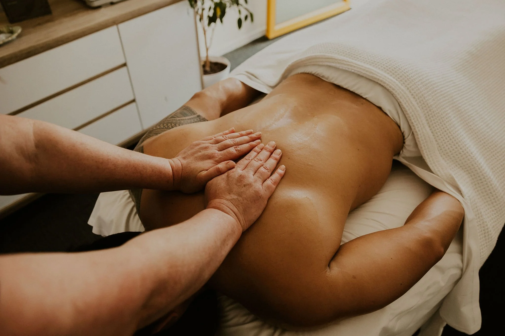 Person receiving a massage on their back in a room with a potted plant and wooden furniture.