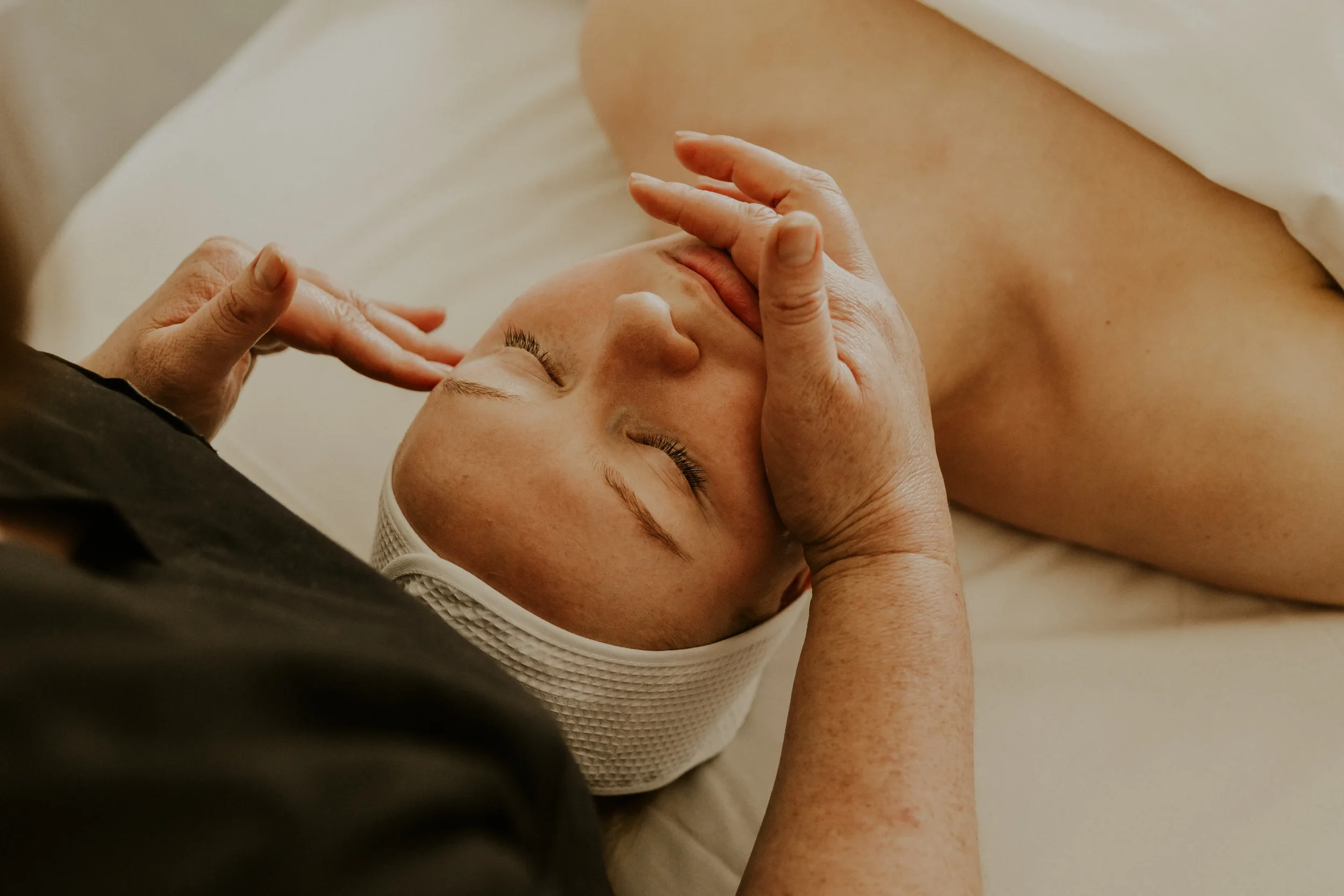 A person receiving a massage on their back, lying face down with hands gently massaging their shoulders and upper back.