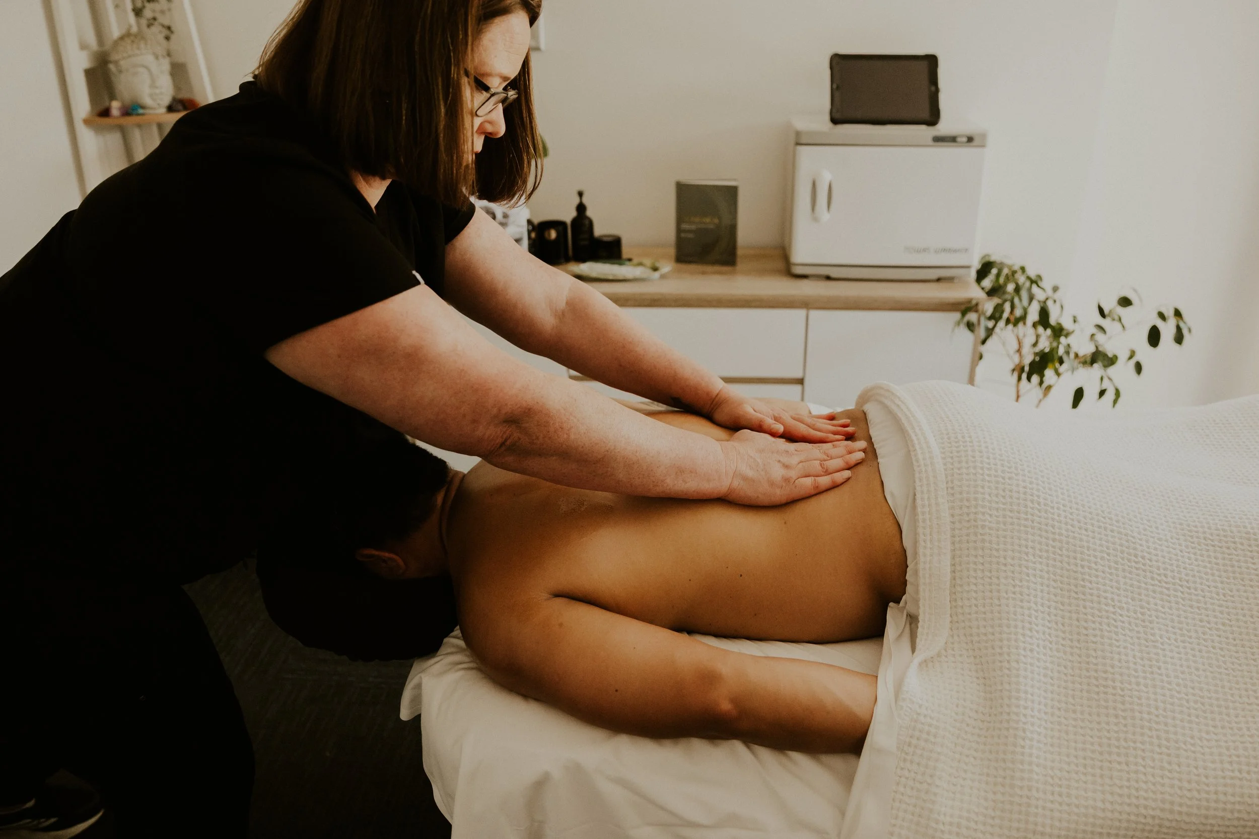 A woman is performing a massage on a person lying face down on a massage table in a therapy room.