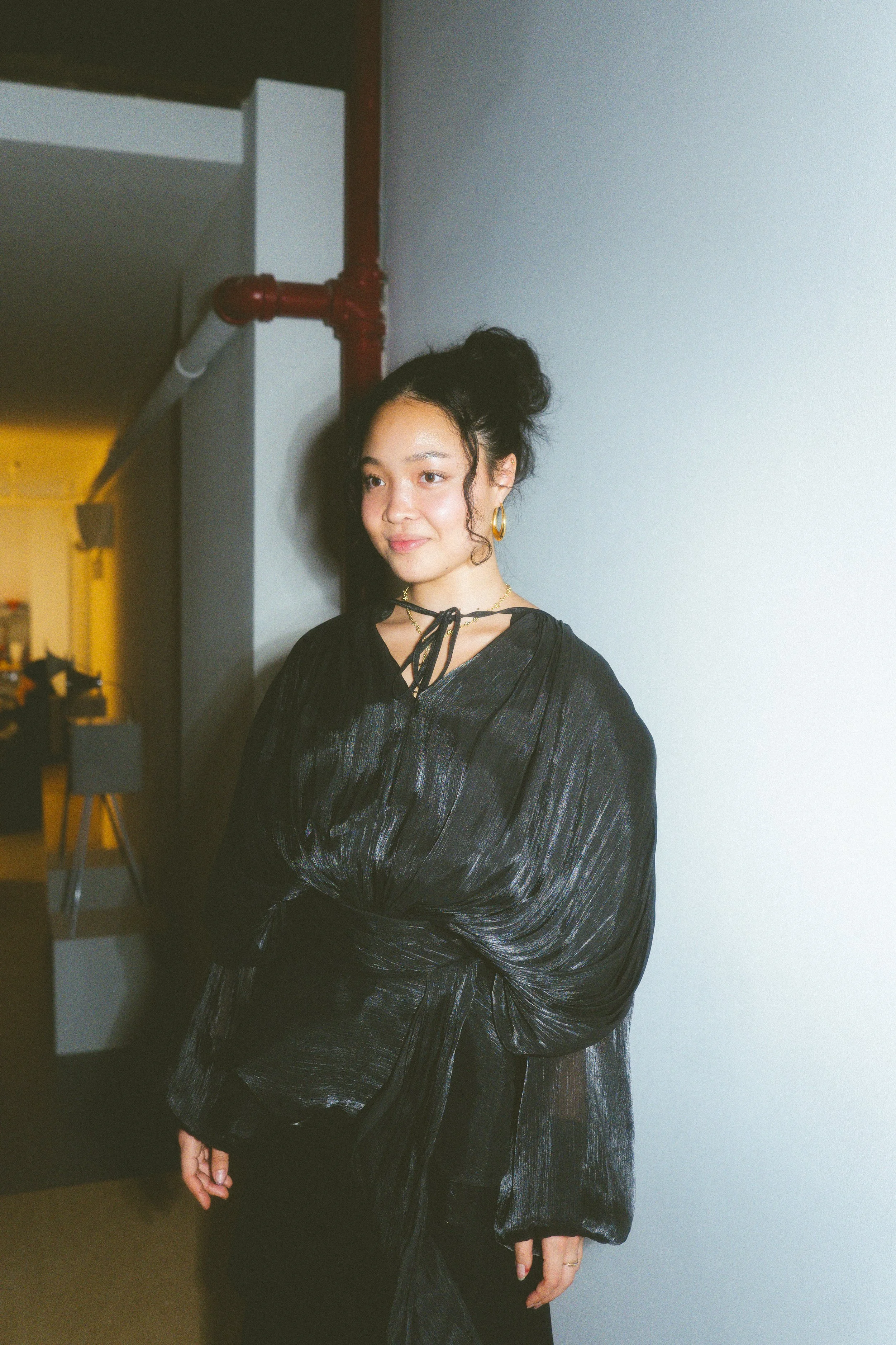 Katie Jones in a black silk blouse, standing against a pale wall