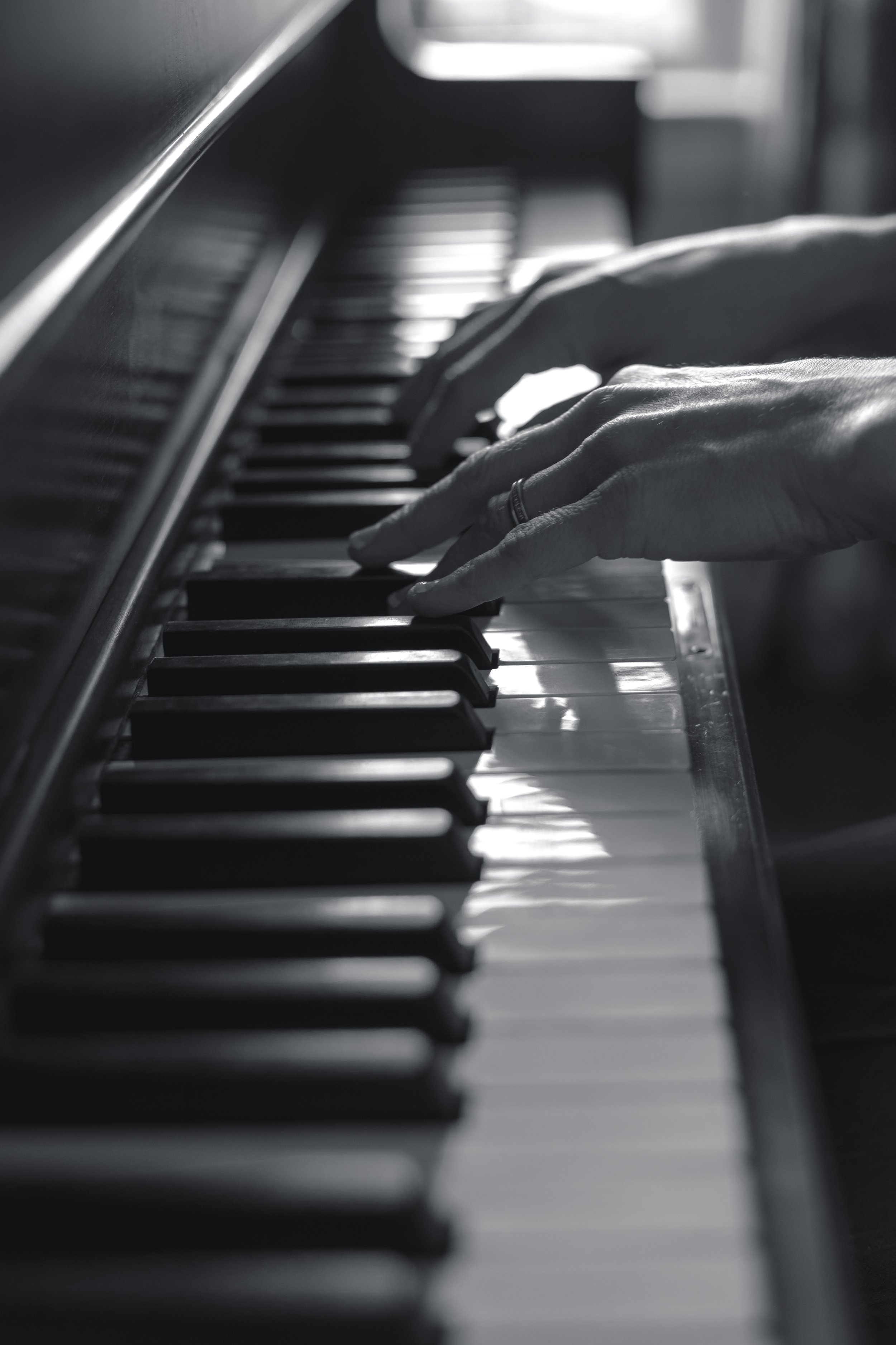 Close-up of a person's hand playing piano keys, with black and white keys visible in black and white photography.