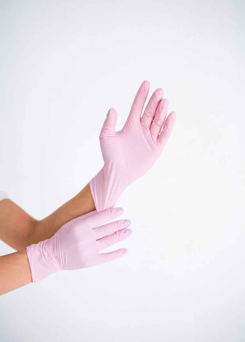 A person putting on light pink medical gloves against a white background.