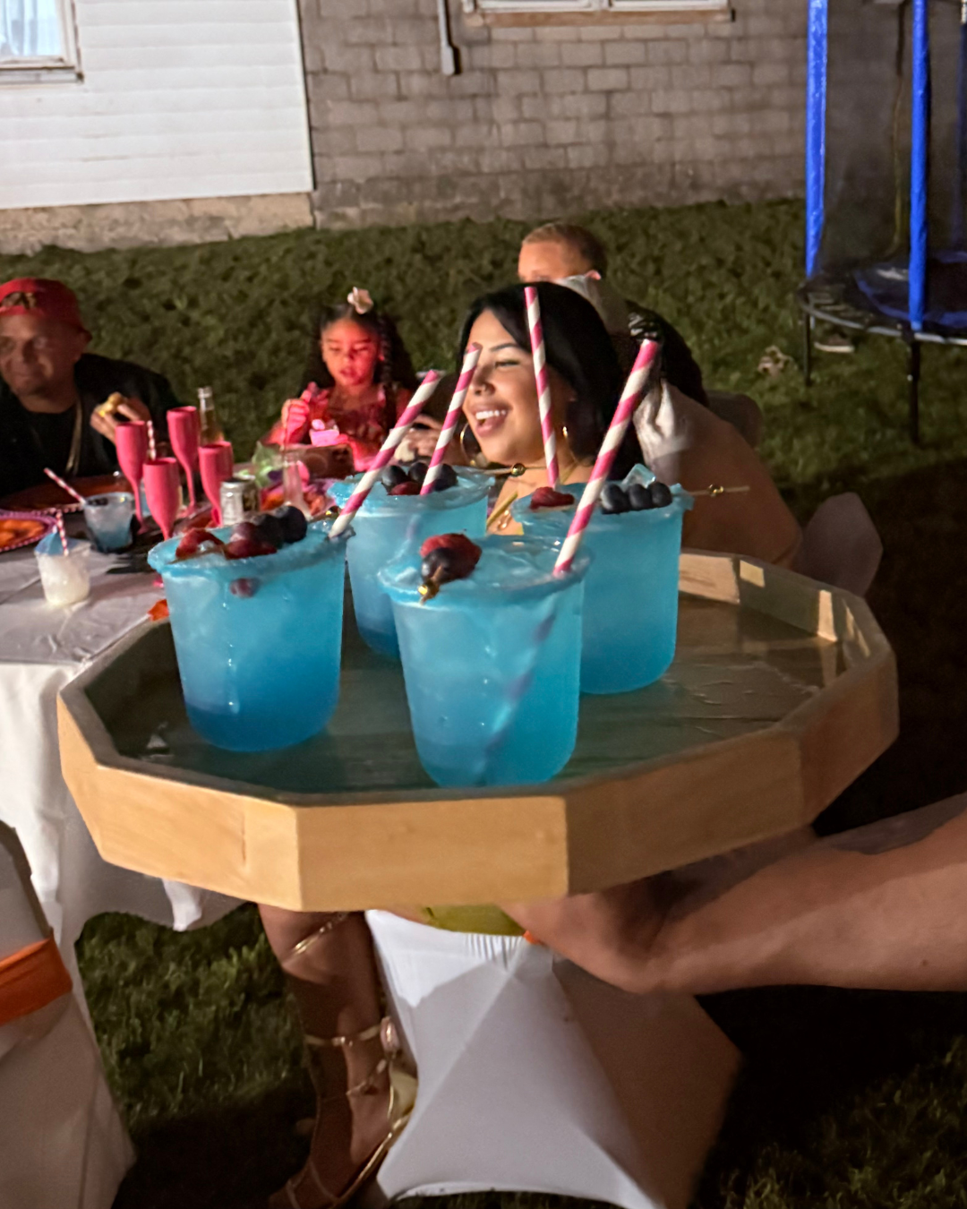 Woman smiling at a birthday celebration with blue cocktails with striped straws on a tray.