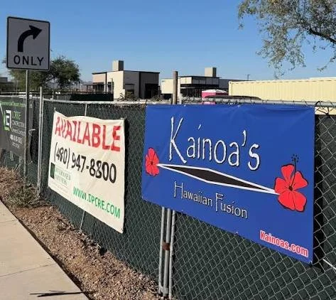Fenced area with two signs: one advertising real estate availability and the other for Kainoa's Hawaiian Fusion restaurant.