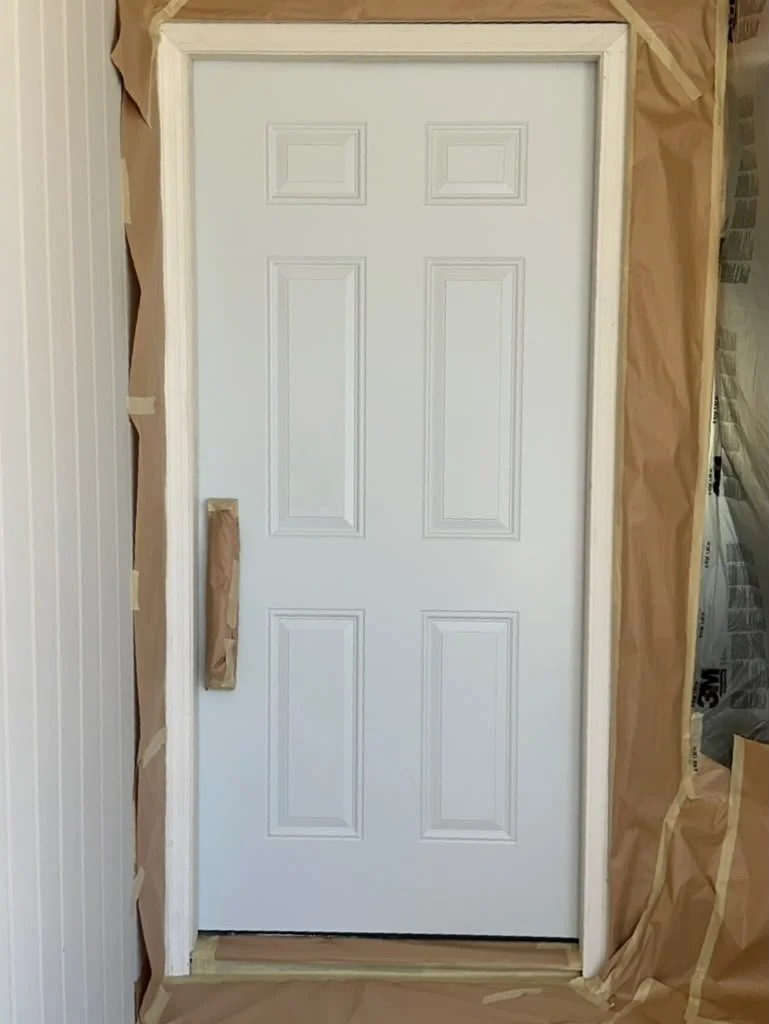 White door with raised panel design, surrounded by painter's paper and tape for painting or renovation.