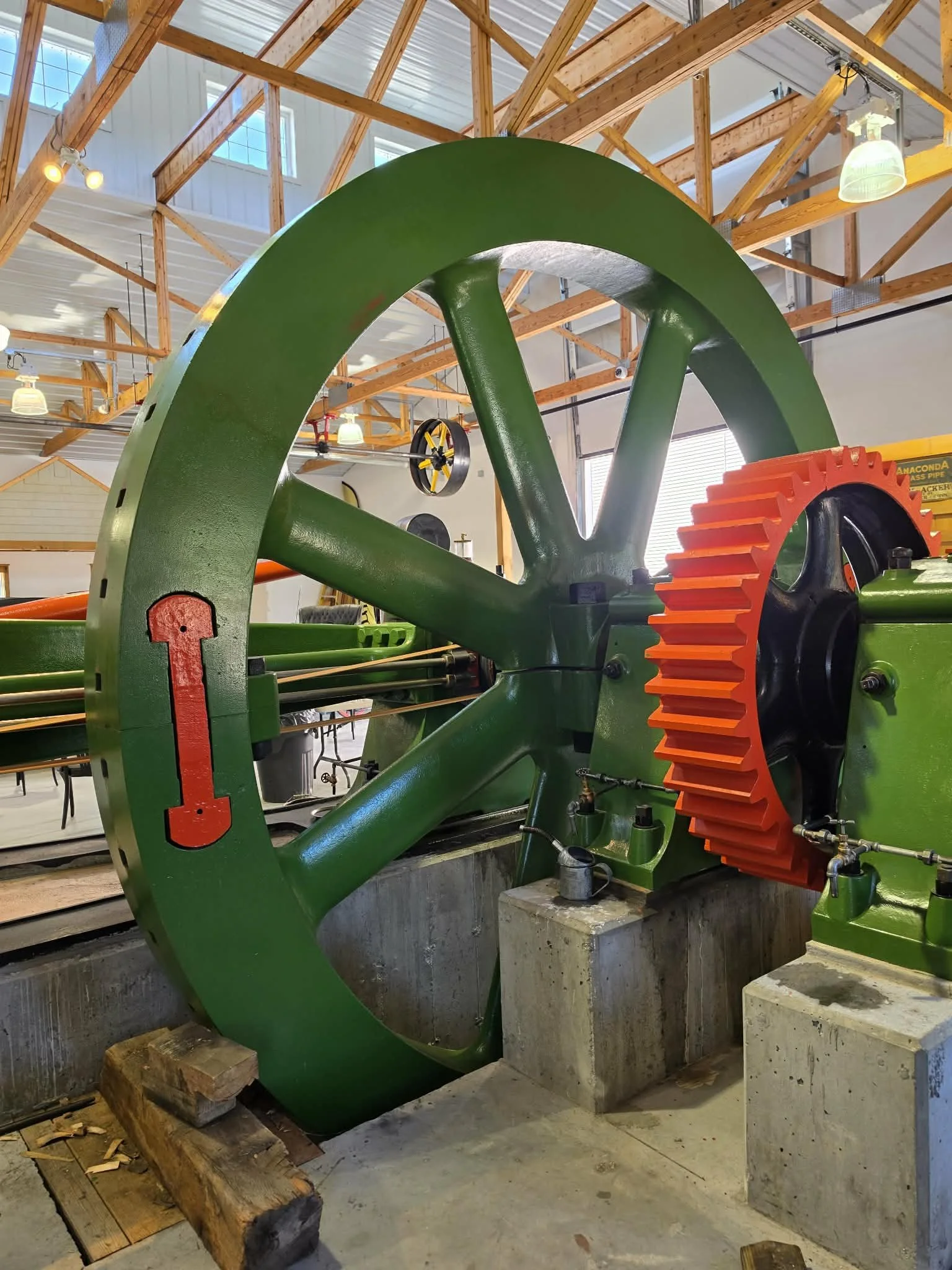 Large green flywheel and red gear from an antique steam engine in an industrial building.