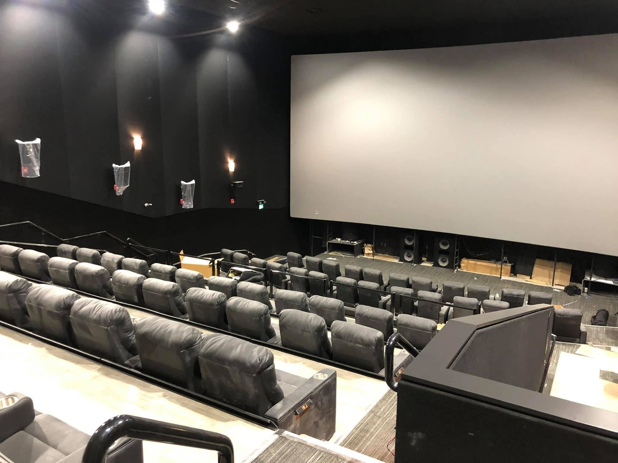 Empty movie theater with rows of black leather seats and a large blank white screen at the front.