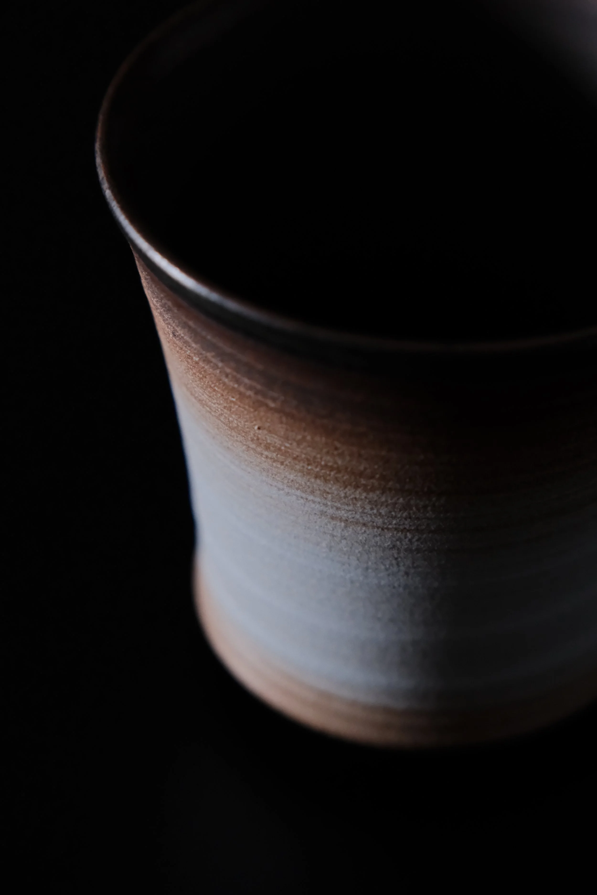 Close-up of the dark inner part of a Japanese ceramic mug with a textured exterior, against a black background.