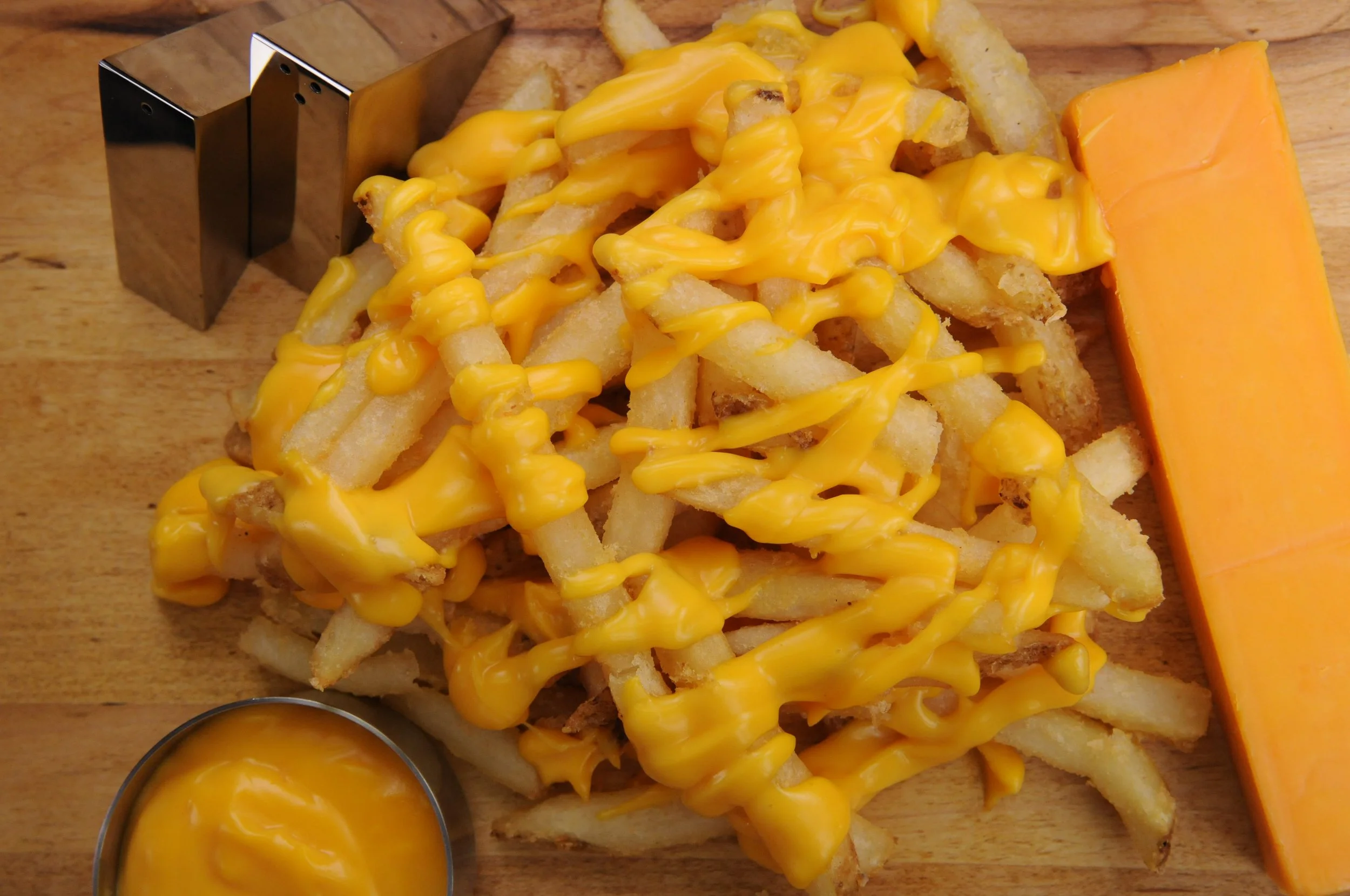 Cooked French fries topped with melted cheddar cheese and served with a side of cheese sauce and a slice of cheddar cheese.
