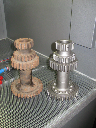 Comparison of rusty and new metal gears on a perforated metal surface.